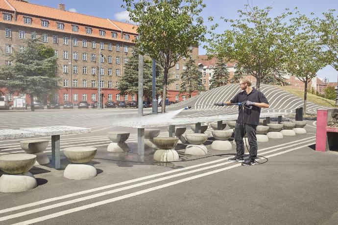 Operator pressure-cleaning an outdoor public plaza area with seating structures